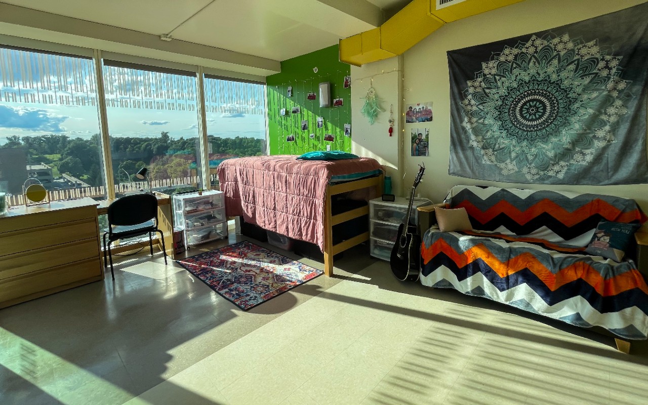 A twin bed, a couch, and a drawer are located in a large room with decorations along the wall. 