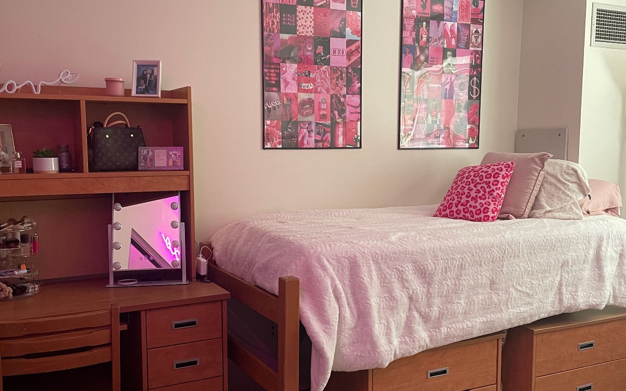 UPA dorm bedroom decorated with pink sheets and pillows and a desk decorated with a light up mirror 