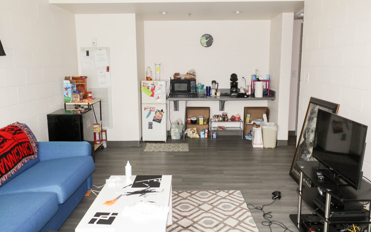 Living room and kitchen area in quad room in Turner Hall. There is a blue sofa on the left and a wide screen TV on the right.